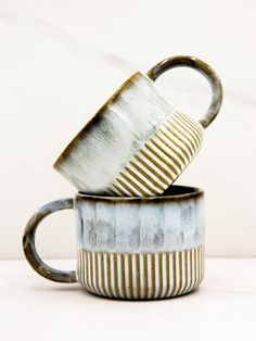 two coffee mugs stacked on top of each other in front of a white wall