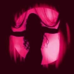 the silhouette of a woman with her arms outstretched in front of a red light and curtains