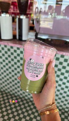 a person holding up a green and pink drink