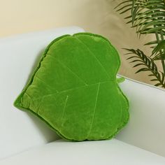 a green leaf shaped pillow sitting on top of a white couch next to a potted plant