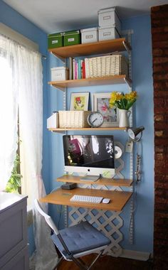 a computer desk sitting under a window next to a shelf filled with books and papers