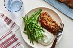 a white plate topped with green beans and meat next to a glass of blue water