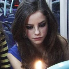 a woman sitting in front of a cake with a lit candle on top of it