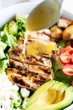 a salad with chicken, avocado and tomatoes is being drizzled with dressing