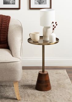 a table with two cups on it next to a chair and pictures hanging on the wall