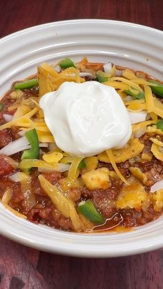 a white bowl filled with chili and sour cream on top of a wooden table next to a fork