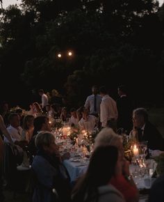 a group of people sitting around a dinner table with candles in the middle of them