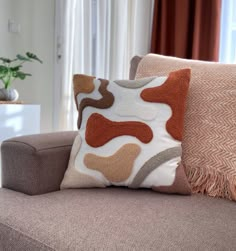 a couch with two pillows on top of it and a vase in the back ground