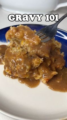 a blue and white plate topped with meat covered in gravy next to a fork