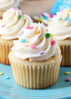 three cupcakes with white frosting and sprinkles on a blue plate