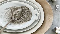 two white plates with silver spoons on top of each one and some ornaments in the background