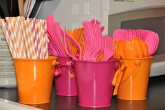 pink and orange cups with utensils in them sitting on a counter next to a microwave