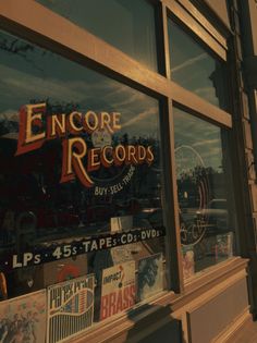 a store front window with various records on it's glass and the reflection of another building in the window