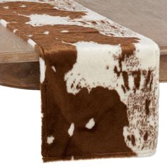 a cow print table runner on top of a wooden table with white and brown spots