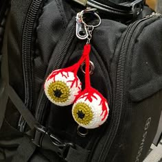 two crocheted eyeballs hanging from a black backpack with red and white trim