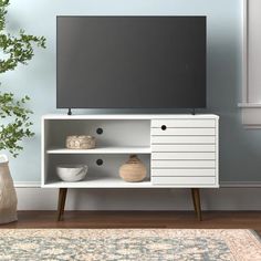 a white entertainment center with shelves and vases on the floor in front of a blue wall