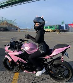 a woman in black catsuit sitting on a pink motorbike and wearing a helmet