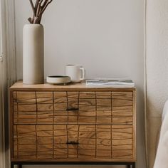 a wooden dresser with a white vase and some branches on it next to a window