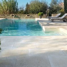 an empty swimming pool with lounge chairs and trees in the backround, surrounded by greenery