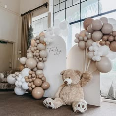 a teddy bear sitting in front of a large balloon arch with balloons attached to it