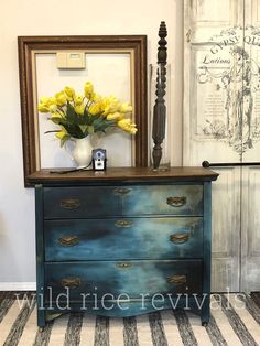 a blue dresser with yellow flowers on top in front of a mirror and framed pictures