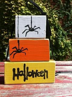 three wooden blocks with halloween painted on them sitting on top of a table in front of some trees