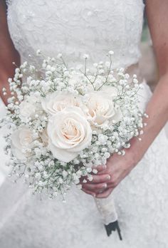 a bride holding a bouquet of white roses and baby's breath in her hands