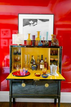 a bar cart with liquor bottles and glasses on it in front of a red wall