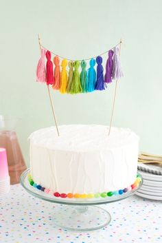 a cake with white frosting and colorful tassels on top is sitting on a table