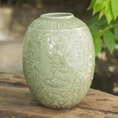 a green vase sitting on top of a wooden table next to a tree branch with leaves