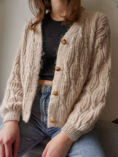 a woman sitting on top of a couch wearing a cardigan sweater and denim jeans