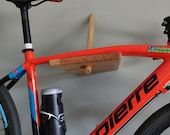 an orange bike is parked in front of a gray wall and has a beer holder attached to the handlebars