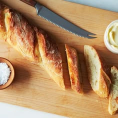 bread and butter on a cutting board next to a knife, spoons and salt