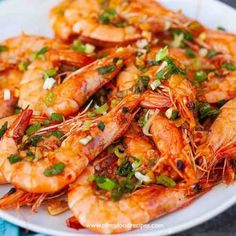 a white plate topped with cooked shrimp and garnished with scallions on top