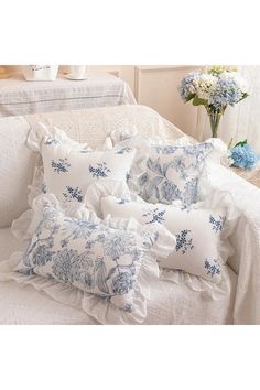 blue and white pillows on a bed with flowers in vases next to the headboard