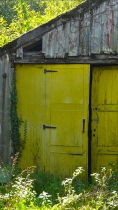 an old barn with two yellow doors in the grass