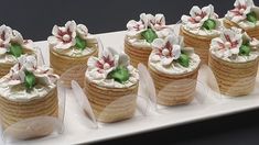 there are many cupcakes with white frosting and flowers on them sitting on a tray