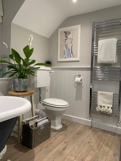 a white toilet sitting next to a bath tub in a bathroom under a painting on the wall