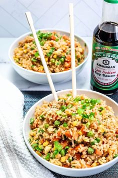 two white bowls filled with rice and vegetables next to a bottle of beer on a table