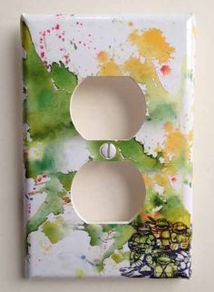 a light switch cover with paint splattered on it and two white outlets in the middle