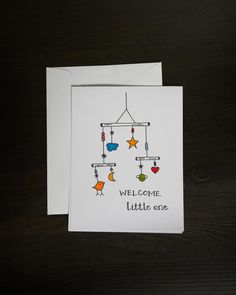 a greeting card with an image of a mobile hanging from it's strings and the words welcome little one