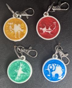 four keychains with different designs on them sitting next to each other in front of a black background