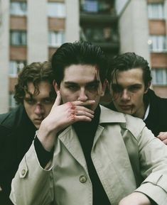 three young men standing in front of a tall building with their hands on their face