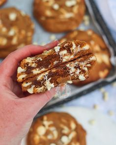 a hand holding up some cookies with white chocolate and walnuts on top in front of them