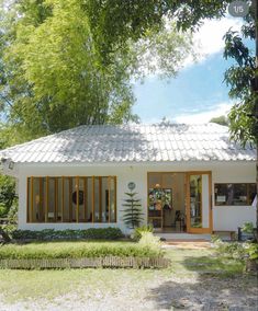 a small white house sitting in the middle of a lush green field next to trees