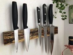 there are five knives hanging on the wall next to each other and one knife holder