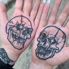 two hand tattoos with skulls and crosses on the palms, one has a compass in it