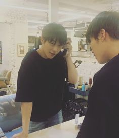 two young men standing in front of a counter talking on their cell phones and looking at each other