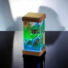 a wooden stand with a small glass vase on it's side and a pond in the middle