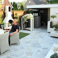 two men sitting in wicker chairs on a patio with stone flooring and landscaping